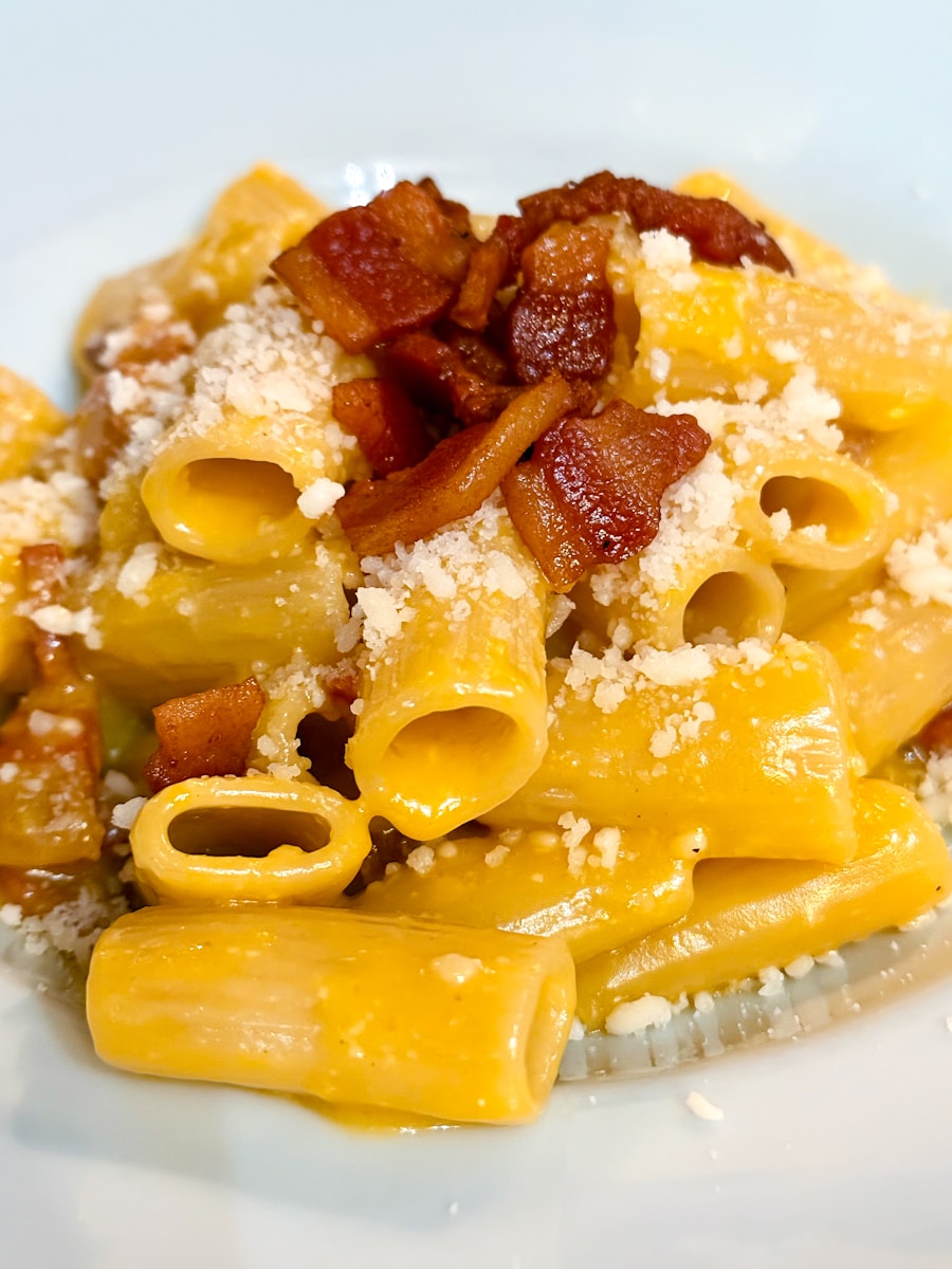 A white plate topped with pasta and bacon